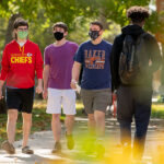 four students in masks walking on campus